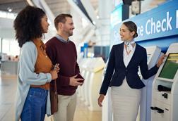 Woman, passenger assistant and couple at airport by self service check in station for information, help or FAQ. Portrait of happy female services agent helping travelers register or book air flight